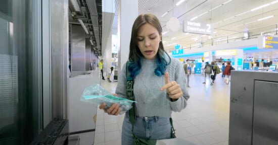 A woman stands in an airport holding a bag of film.
